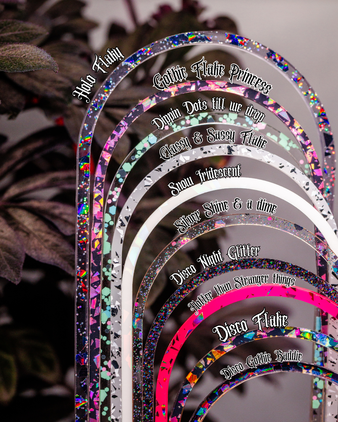 A set of arched, acrylic with colorful confetti and holographic speckles, each labeled with a different disco-themed name or phrase like 'Halo Flare,' 'Gallic Flare Princess,' 'Dancing Do Us All,' 'Classic & Sexy Flare,' 'Raw Tristential,' 'Sugar Shine & a dime,' 'Disco Night Glitter,' 'Hysteria Stranger things,' and 'Disco Flare.' The plates are arranged in a fan-like stack against a dark, blurred background with foliage.